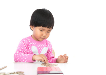 白背景前小女孩正在摆弄桌子上的欧元硬币以及桌子上还有计算器