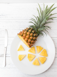 白色碟子上一个切开的金钻凤梨（无眼菠萝）和一把刀子