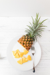白色碟子上一个切开的金钻凤梨（无眼菠萝）和一个叉子