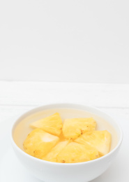 白色木纹背景上的一碗正在泡盐水的菠萝肉侧视