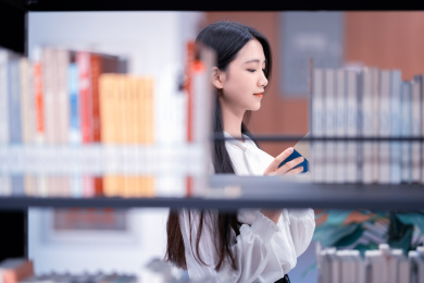   漂亮的女生站在图书馆书架旁边