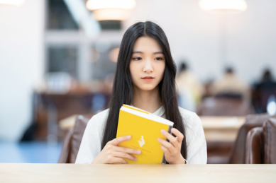 漂亮的女生坐在图书馆书桌前看书