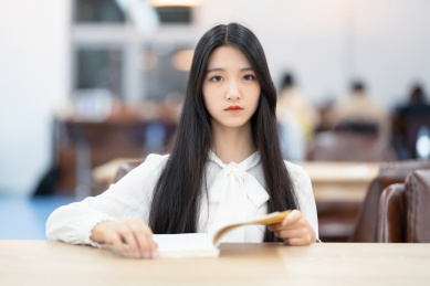  漂亮的女生坐在图书馆书桌前翻书