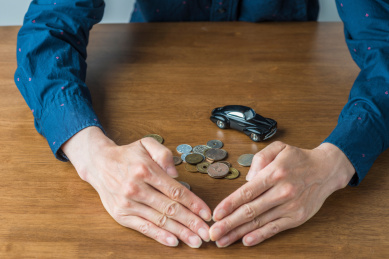 实木桌面上被双手拢住的钱币和复古汽车模型