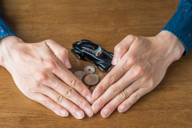 实木桌面上被双手拢住的钱币和复古汽车模型