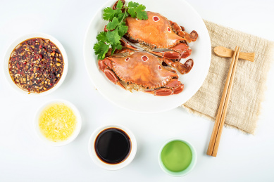 一碟清蒸三点蟹和醮料酒水在白背景上