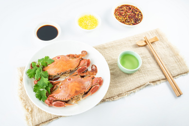 一碟清蒸三点蟹和醮料酒水在白背景上