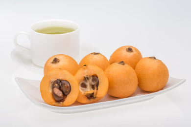 白色背景下茶杯前长条餐盘里的黄色枇杷果