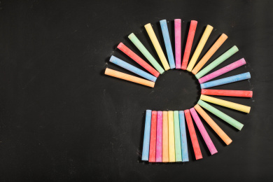 围成开放式圆的彩色粉笔放在黑色黑板上