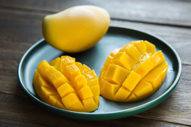 一个完整的芒果和切好的芒果放在木桌上的绿色盘子里