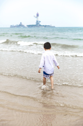 蓝天白云海边浅滩玩水的男童背影