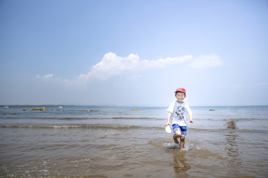 蓝天白云海边浅滩玩水的男童