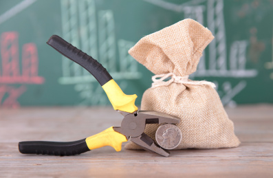 画着金融图形的黑板前一麻袋资金和一把钳子夹着一枚美元硬币