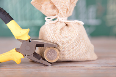 画着金融图形的黑板前一麻袋资金和一把钳子夹着一枚欧元硬币