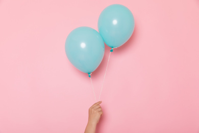 粉色背景上一只手拿着两个蓝色气球