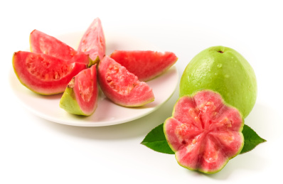 一个完整的和一个有切面的新鲜红心芭乐后有一盘切开的红心芭乐果瓣