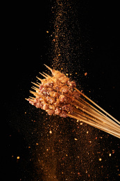 黑色背景上撒调料的烤羊肉串