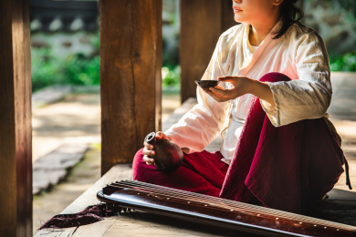 身着汉服女子坐在中式房子阳台上拿着酒杯酒壶喝酒地板上放着一把古琴