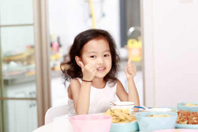 在家里餐桌前吃完饭的小女孩双手竖起大拇指