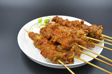 香喷喷的烤好的羊肉串，白色带花纹的瓷盘及灰色的台面