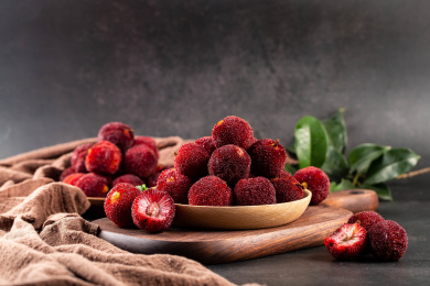 暗色背景里的木板上碟装新鲜杨梅