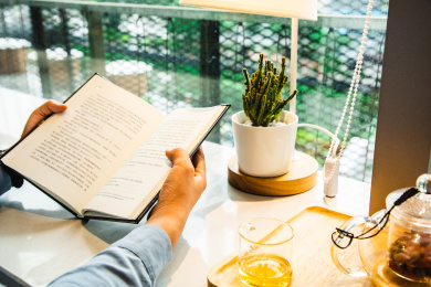 特写女性双手翻开一本书阅读桌上放着一壶花茶和茶杯