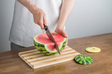 手拿三德刀在拼竹砧板上切西瓜