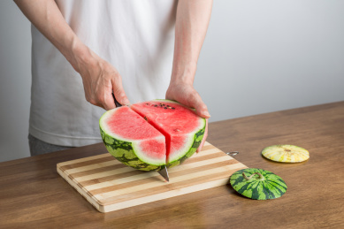 手拿三德刀在拼竹砧板上切西瓜