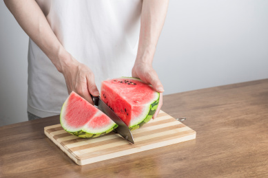 手拿三德刀在拼竹砧板上切西瓜