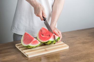 手拿三德刀在拼竹砧板上切西瓜