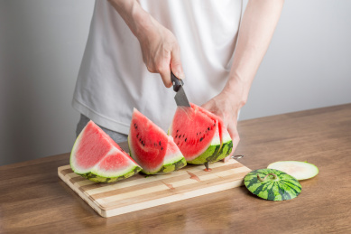 手拿三德刀在拼竹砧板上切西瓜