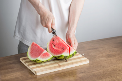 手拿三德刀在拼竹砧板上切西瓜