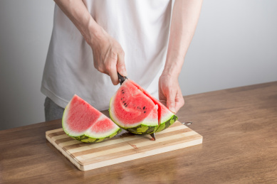 手拿三德刀在拼竹砧板上切西瓜