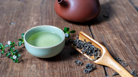 一个紫砂壶和装着茶水的汝窑茶杯放在旧木板上