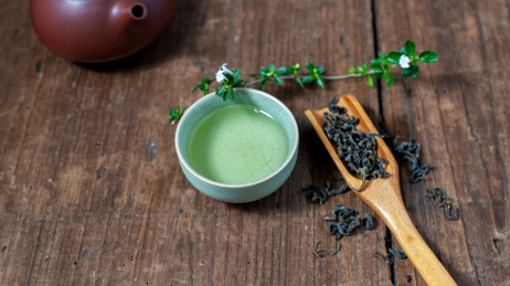 一个紫砂壶和装着茶水的汝窑茶杯放在旧木板上