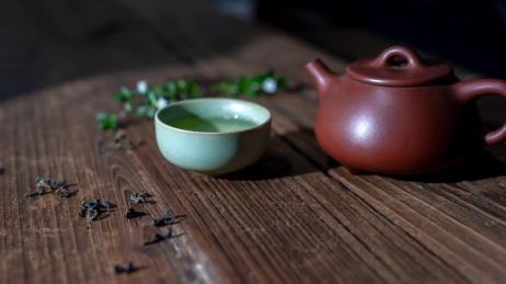 一个紫砂壶和装着茶水的汝窑茶杯放在旧木板上