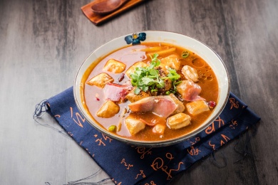 蓝色餐布上有一碗红汤火腿豆泡汤