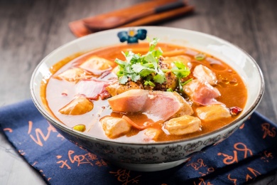 蓝色餐布上有一碗红汤火腿豆泡汤