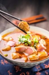 蓝色餐布上有一碗红汤火腿豆泡汤