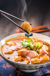蓝色餐布上有一碗红汤火腿豆泡汤