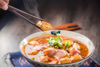 蓝色餐布上有一碗红汤火腿豆泡汤