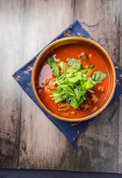 蓝色餐布上有一碗砂锅番茄汁牛杂汤锅