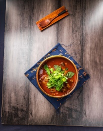 蓝色餐布上有一碗砂锅番茄汁牛杂汤锅