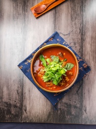 蓝色餐布上有一碗砂锅番茄汁牛杂汤锅