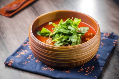 蓝色餐布上有一碗砂锅番茄汁牛杂汤锅