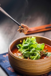 蓝色餐布上有一碗砂锅番茄汁牛杂汤锅