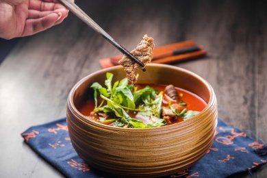 蓝色餐布上有一碗砂锅番茄汁牛杂汤锅