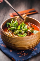 蓝色餐布上有一碗砂锅番茄汁牛杂汤锅