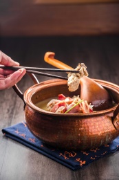 黑色餐布上的一口铜锅火腿炖柴鸡