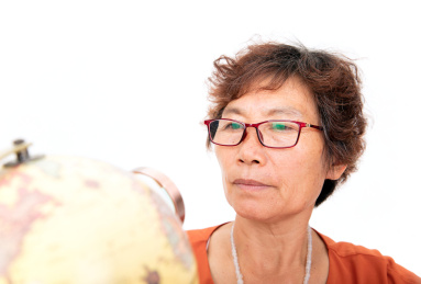 一位带着眼镜亚洲面孔的女性老年人正拿着放大镜在地球仪上观察